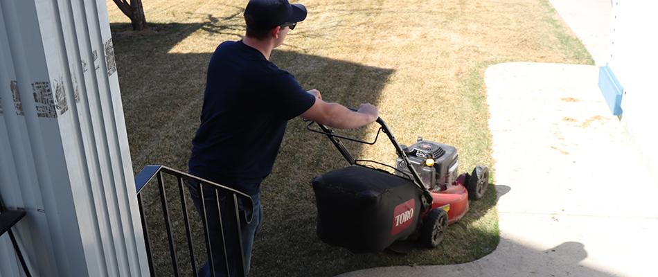 Prestige Outdoor Services professional using a push mower on a customer's lawn in Calgary, AB.
